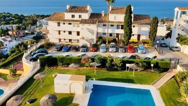 Un hotel con piscina, diverse auto parcheggiate davanti e vista sul mare.