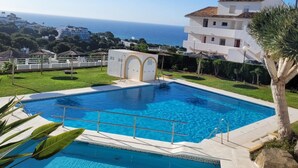 Una piscina con vista chiara sul mare sullo sfondo, circondata da un prato curato e un edificio bianco con tetto in tegole.