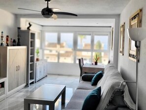 A modern living room with a sofa, coffee table, and a dining area with a table and chairs. - Sunstay Flat Centauro Mijas (Mijas)