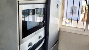 Una cucina con forno a incasso e microonde, una finestra con inferriate e vista su un edificio.