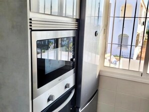 A kitchen with a built-in oven and microwave, a window with bars, and a view of a building outside. - Sunstay Flat Centauro Mijas (Mijas)