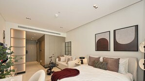 A modern bedroom with a large bed, a bedside table, a chair, and a desk. There is a plant on the desk and a mirror on the wall. - Bloomfields Studio in NAS3 - Arjan Dubai (Dubai)