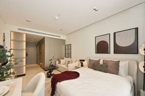 A modern bedroom with a large bed, a bedside table, a chair, and a desk. There is a plant on the desk and a mirror on the wall. - Bloomfields Studio in NAS3 - Arjan Dubai (Dubai)