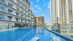 A swimming pool with a lounge chair, surrounded by modern high-rise buildings. - Bloomfields Studio in NAS3 - Arjan Dubai (Dubai)