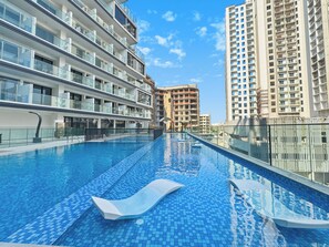 A swimming pool with a lounge chair, surrounded by modern high-rise buildings. - Bloomfields Studio in NAS3 - Arjan Dubai (Dubai)