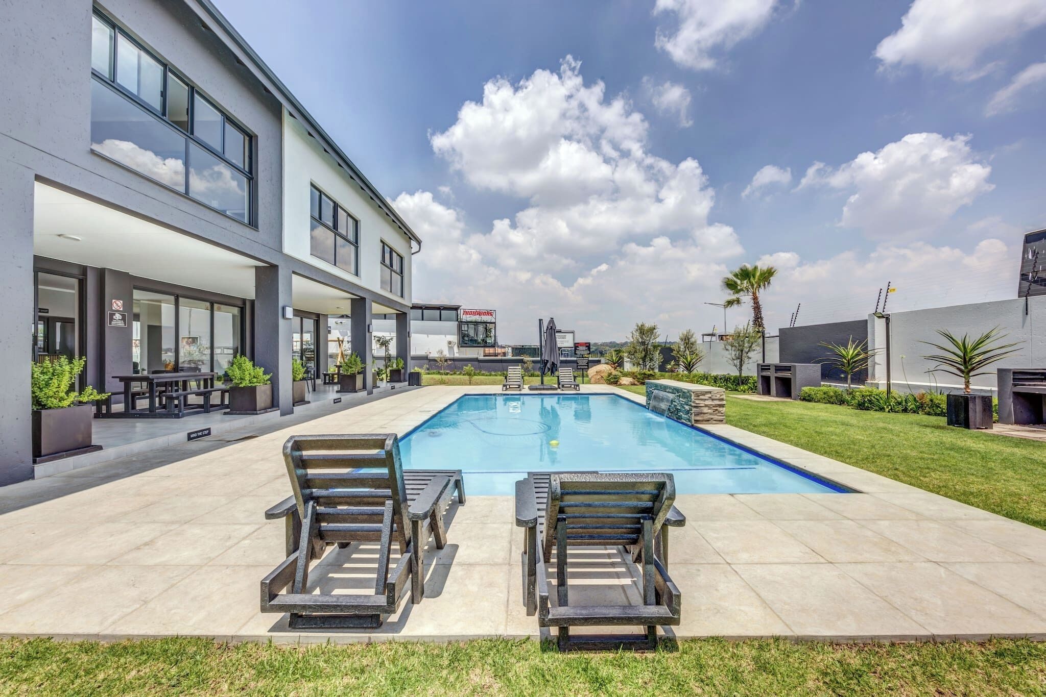 A modern building with a swimming pool, outdoor seating, and a clear sky.