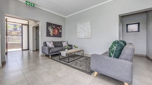 Un salon moderne avec un canapé gris, une table basse et un tapis. Un tableau orne le mur et une fenêtre offre une vue dégagée.