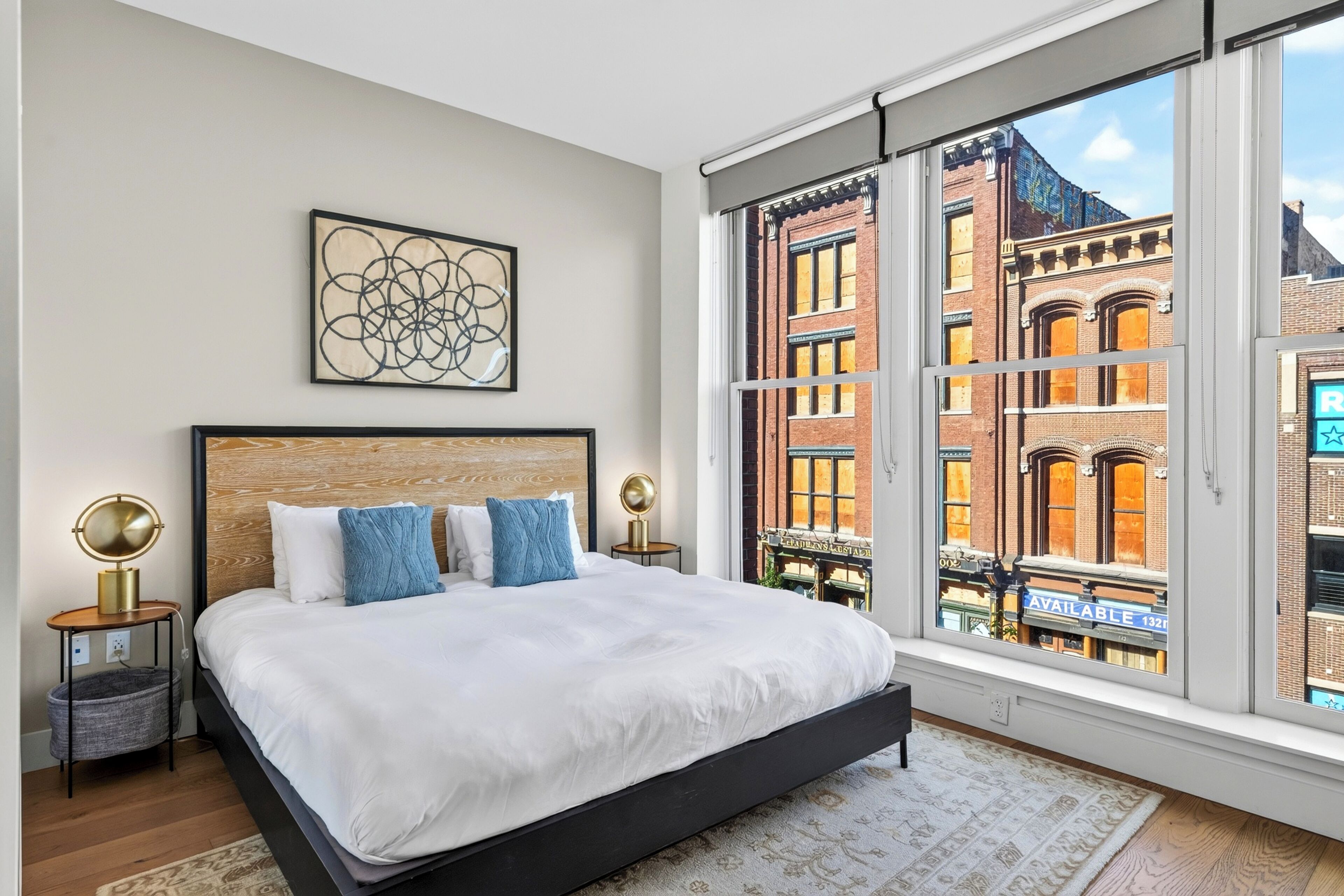 Un dormitorio con una cama grande, vistas a la ciudad a través de ventanales del suelo al techo y una obra de arte enmarcada en la pared.