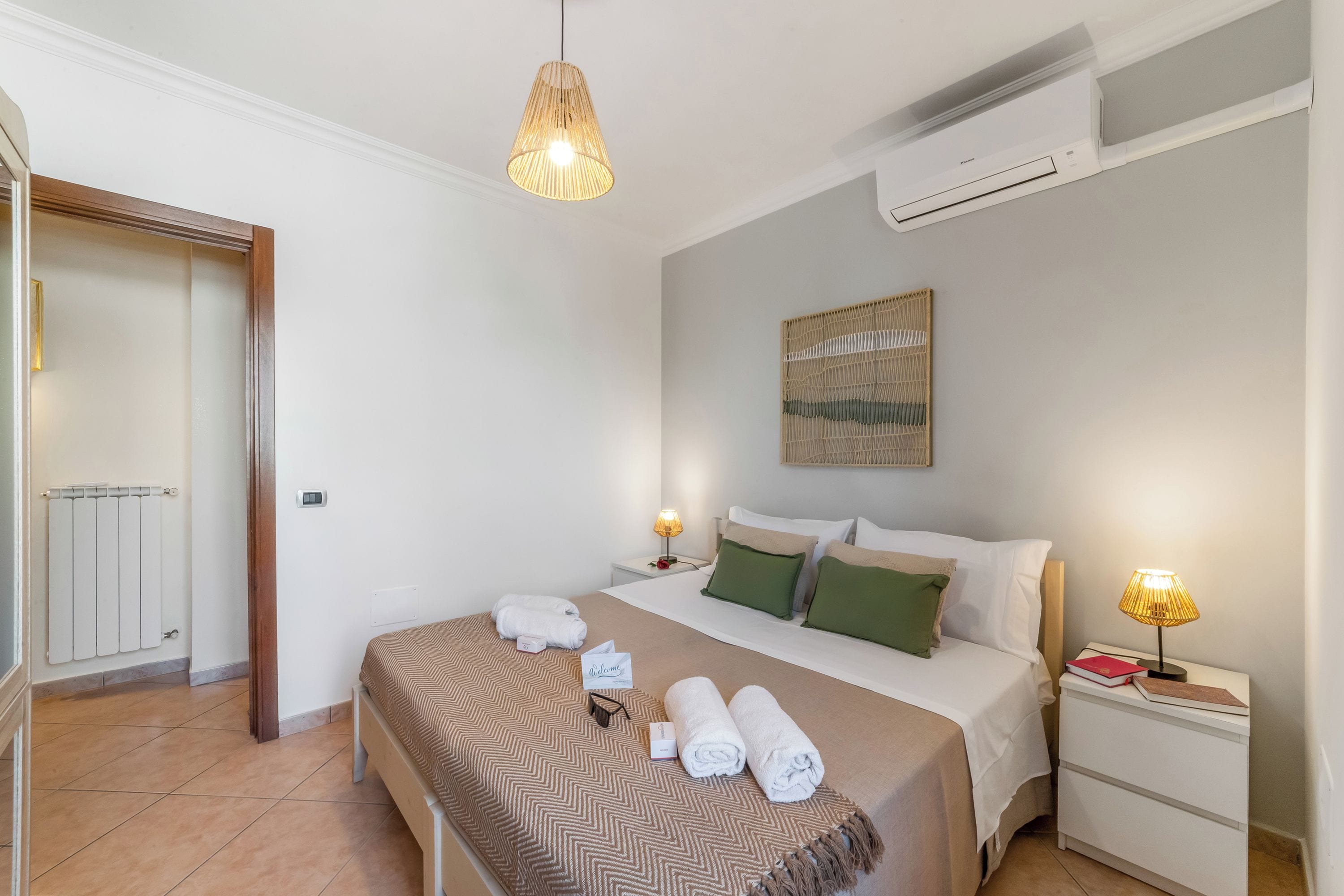 Une chambre d’hôtel comprenant un lit, des tables de chevet, un climatiseur fixé au mur et un luminaire suspendu.