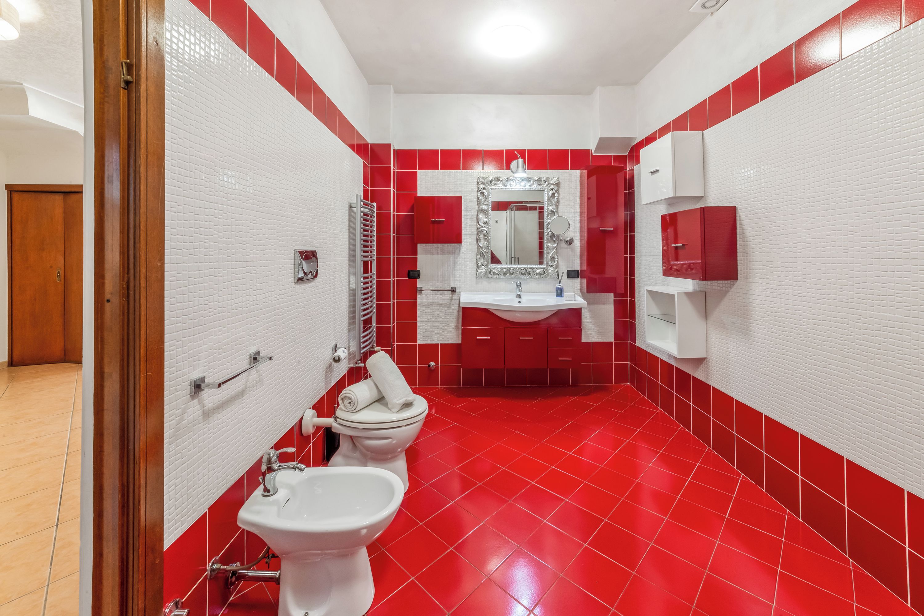 Une salle de bain avec un sol carrelé en rouge et blanc, un lavabo blanc, des toilettes et un bidet.
