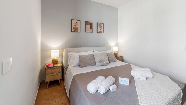Un dormitorio con una cama, dos mesitas de noche, una mesita auxiliar, una lámpara y un aplique de pared.