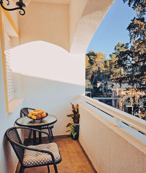 Ein Balkon mit Tisch, Stühlen, einem Blumentopf und Blick auf Bäume und Häuser.