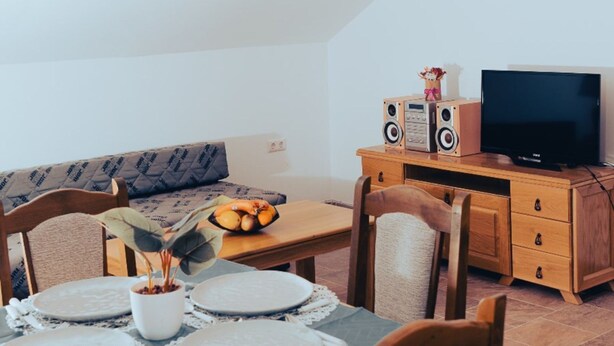 A cozy living room with a dining table set for two, a sofa, a television, and a wooden cabinet with speakers. - Hvar spa & Apartments-superior 1 Bedroom Apartment (Jelsa)