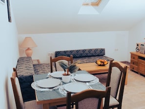 Ein gemütlicher Essbereich mit einem für vier Personen gedeckten Tisch, einer Couch, einer Lampe und einem Lautsprecher.