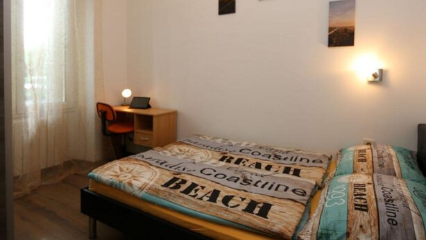 Un dormitorio con cama, escritorio, silla y una lámpara de pared.