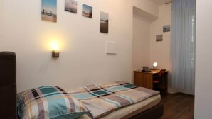 Un dormitorio con cama, escritorio con lámpara y ventana con cortinas.