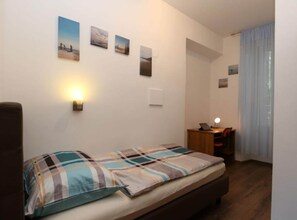 Ein Schlafzimmer mit einem Bett, einem Schreibtisch mit Lampe und einem Fenster mit Vorhängen.