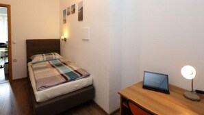Un dormitorio con cama, escritorio, laptop y luz en la pared.