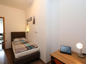 Ein Schlafzimmer mit einem Bett, einem Schreibtisch, einem Laptop und einer Wandleuchte.