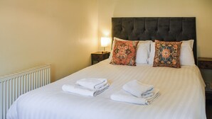 A neatly made bed with white linens and folded towels, a dark upholstered headboard, and decorative pillows with intricate patterns.