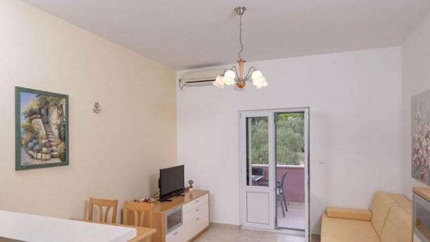 Un ambiente compatto con angolo cottura, zona pranzo, divano e una porta vetrata scorrevole che dà su uno spazio esterno.