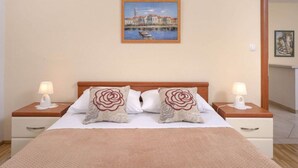 Una camera d'albergo con un letto, due comodini con lampade, un quadro appeso al muro e una porta che dà su un'altra stanza.
