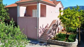 Un edificio rosa con tetto in tegole rosse, una scalinata che conduce a un ingresso coperto e un cielo sereno.