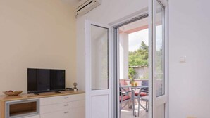 Una stanza con una televisione su un mobile in legno, una porta scorrevole in vetro che dà su un’area esterna con un tavolo e sedie.