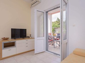 A room with a television on a wooden cabinet, a sliding glass door leading to an outdoor seating area with a table and chairs. - One Bedroom Apartment With Balcony 3 (Jelsa)