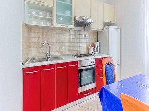 Eine kleine Küche mit roten Schränken, einer Edelstahlspüle, einer Kaffeemaschine und einem Backofen.