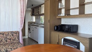 A compact kitchen with a dining table, wooden cabinets, and a microwave. - Country Bungalow (Saint-Georges-de-Reintembault)