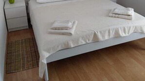Une chambre avec un lit simple, un lit blanc, une table de chevet avec une lampe, un tableau au mur et un plancher en bois.
