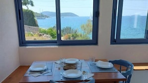 Un coin repas avec une table dressée pour deux personnes, deux chaises et une vue sur la mer grâce à de grandes fenêtres.
