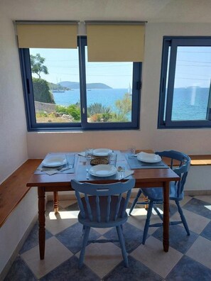 A dining area with a table set for two, two chairs, and a view of the sea through large windows. - Apartments Blaza - Duplex Two Bedroom Apartment (Vodice)