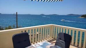 Un balcon avec vue sur la mer, deux chaises et une table recouverte d’une nappe à motifs.