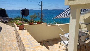Une terrasse en pierre offrant une vue sur la mer, un barbecue et des plantes en pot.
