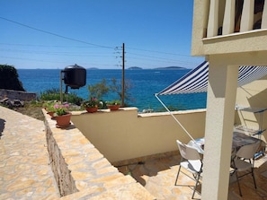 A stone patio with a view of the sea, a barbecue grill, and potted plants. - Apartments Blaza - Duplex Two Bedroom Apartment (Vodice)