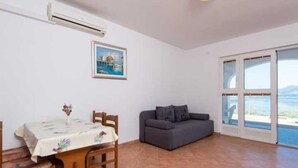 A room with a dining table, a gray sofa, a painting, and a large window with a view. - One Bedroom Apartment With Terrace and Sea View (Ston)