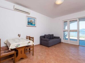 A room with a dining table, a gray sofa, a painting, and a large window with a view. - One Bedroom Apartment With Terrace and Sea View (Ston)