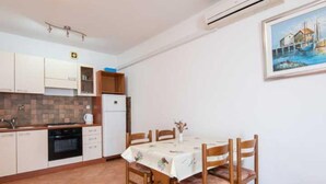 A compact kitchen with white cabinets, a built-in oven, and a dining table with chairs. - One Bedroom Apartment With Terrace and Sea View (Ston)