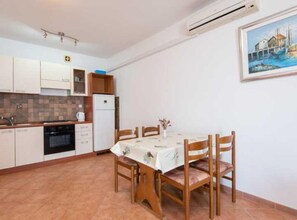 A compact kitchen with white cabinets, a built-in oven, and a dining table with chairs. - One Bedroom Apartment With Terrace and Sea View (Ston)