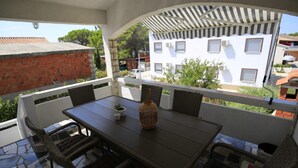 A covered outdoor seating area with a table and chairs, a potted plant, and a view of a white building with windows. - Apartment Barbara - Two Bedroom Apartment With Terrace (Vir)
