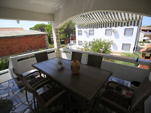 A covered outdoor seating area with a table and chairs, a potted plant, and a view of a white building with windows. - Apartment Barbara - Two Bedroom Apartment With Terrace (Vir)