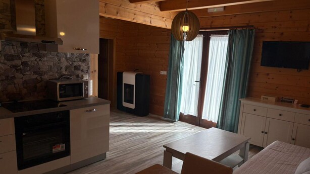 A compact kitchen with a stone backsplash, a microwave, a built-in oven, and a wooden dining area with a table and chairs. - Apartments Plitvice Forest - Superior One Bedroom Apartment With Terrace (Plitvicka Jezera)
