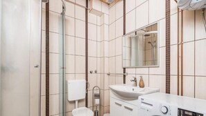 A modern bathroom with a glass shower enclosure, a toilet, a sink with a mirror, and a front-loading washing machine. - Apartments Plitvice Forest - Superior One Bedroom Apartment With Terrace (Plitvicka Jezera)