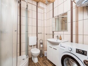 Ein modernes Badezimmer mit Duschkabine aus Glas, Toilette, Waschbecken mit Spiegel und einer Waschmaschine mit Frontlader.