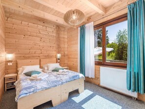 Ein Schlafzimmer einer Holzhütte mit einem Bett, zwei Nachttischen, einer Pendelleuchte und einem Fenster mit Vorhängen.