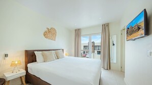 A hotel room with a large bed, bedside lamps, a heart-shaped wall decoration, a painting, and a view of buildings outside. - Luxury 3BR Pool Villa • 3 Baths • Villa Twin B (Noord)