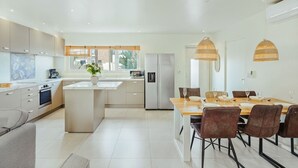 A modern kitchen with a central island, a dining area with a wooden table and chairs, and a large window providing natural light. - Luxury 3BR Pool Villa • 3 Baths • Villa Twin B (Noord)