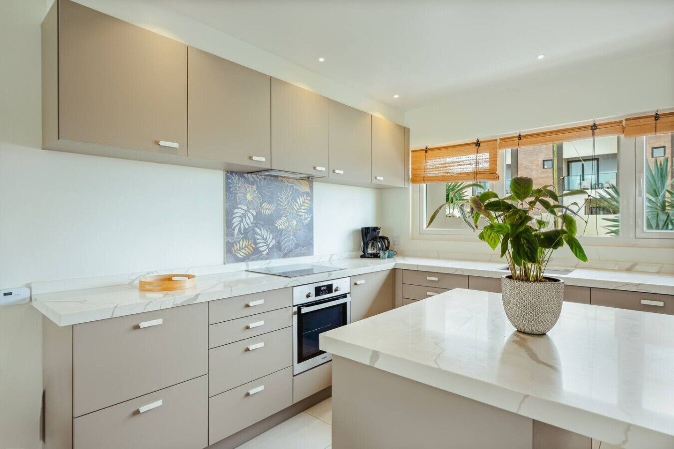 Uma cozinha moderna com ilha central, eletrodomésticos embutidos e uma janela ampla com persianas.